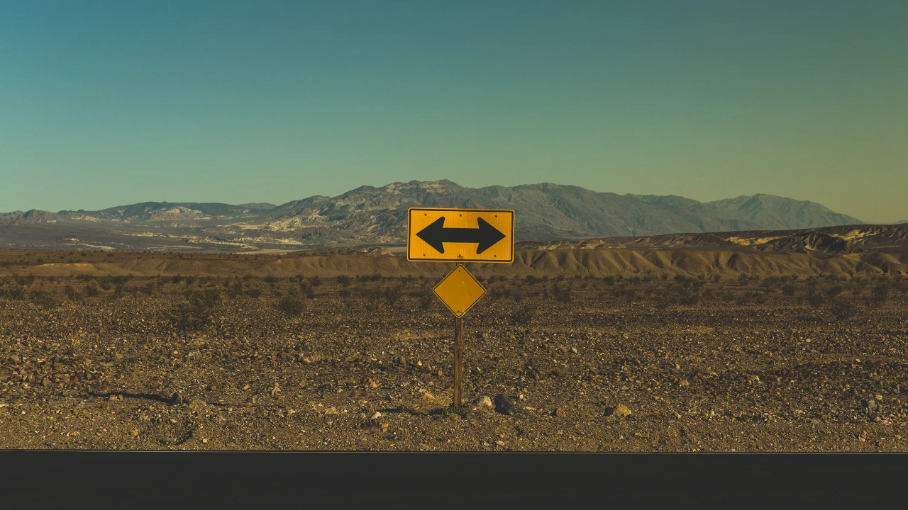 A yellow sign with a black arrow on a desert backdrop.