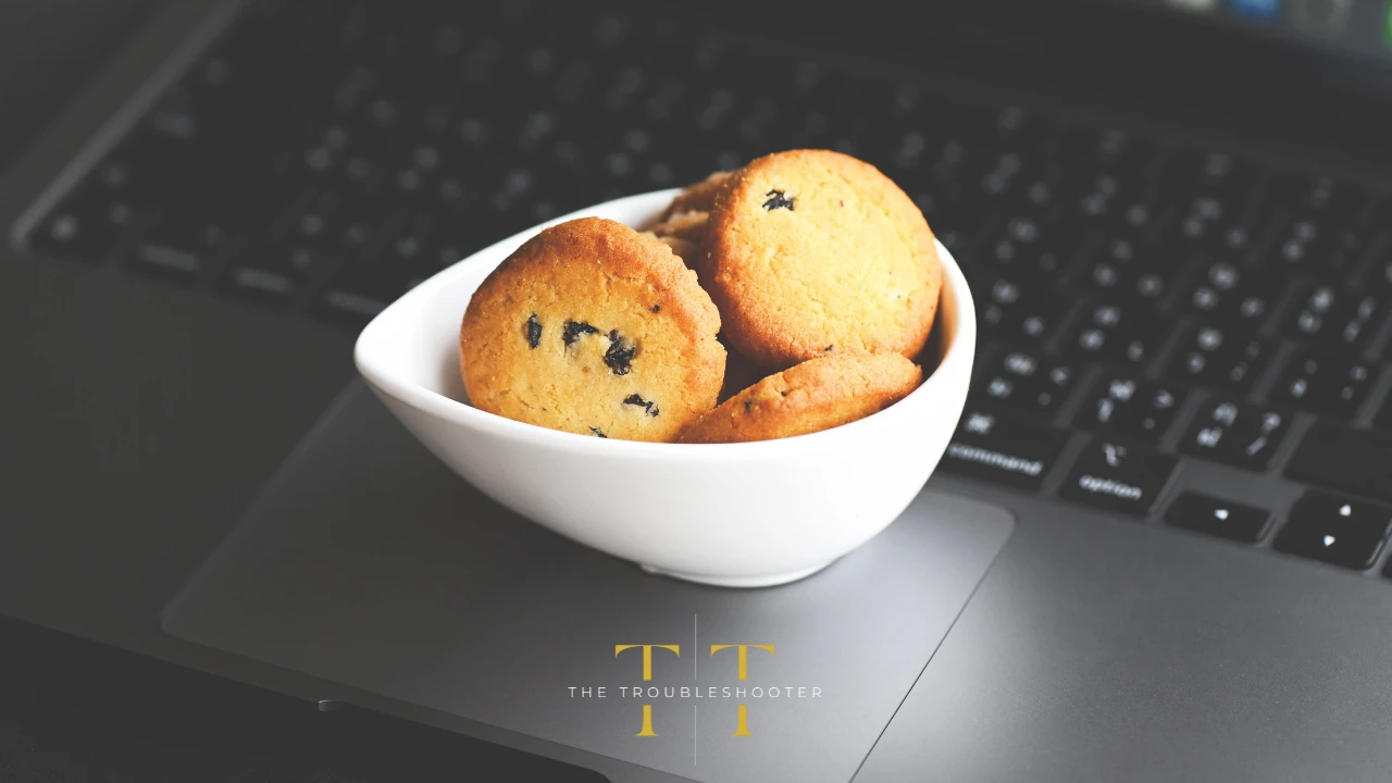 A bowl of cookies sits on an open laptop. The Troubleshooter logo in the foreground.