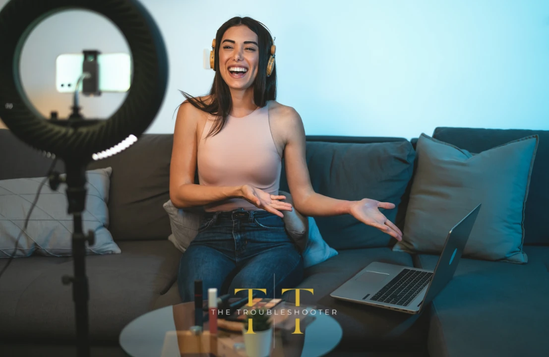 A woman sits smiling on a sofa in front of a spotlight and laptop. The Troubleshooter logo in the foreground.