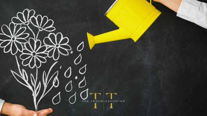 A yellow watering can on a black chalkboard background next to an illustration of drops of water pouring on flowers. The Troubleshooter logo in the foreground.